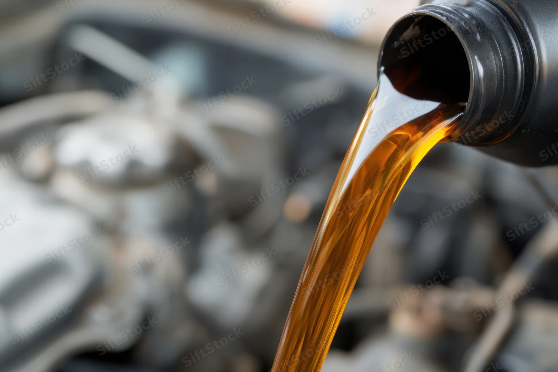 Engine oil pouring from a black bottle into a car engine during maintenance