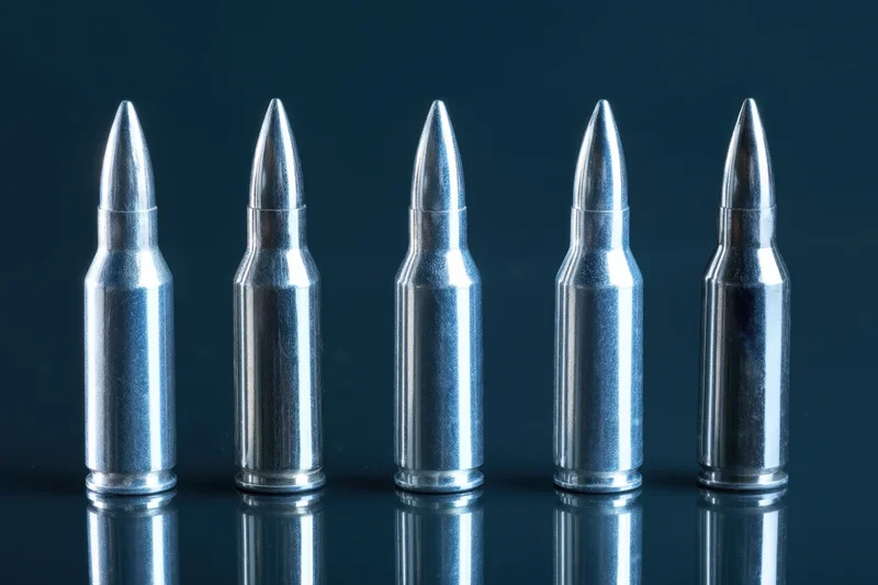 Five metallic bullets arranged in a row on a reflective dark surface
