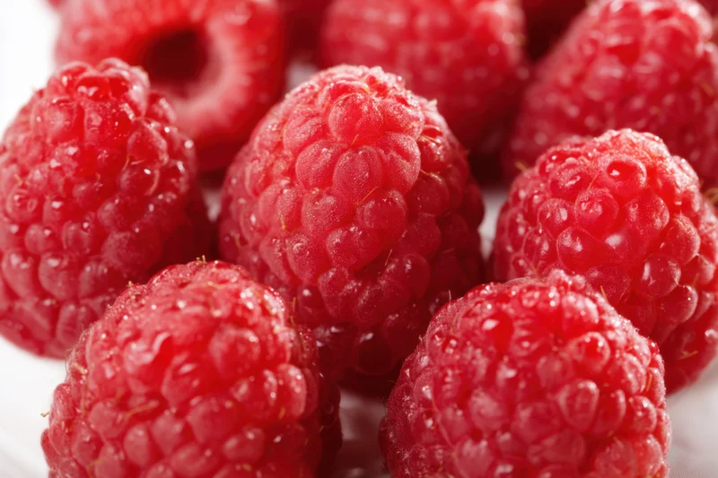 Fresh plump raspberries arranged in a cluster on a white surface