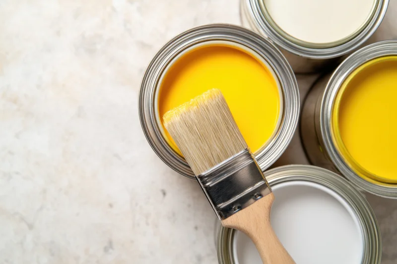 Open paint cans with a brush resting on one, arranged on a light marble surface