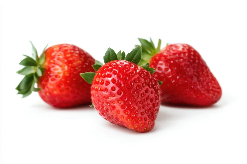 Three fresh ripe strawberries arranged on a white surface with green leaves and seeds visible