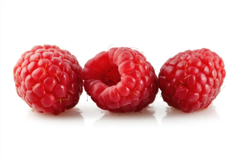 Three fresh raspberries arranged in a line on a white surface