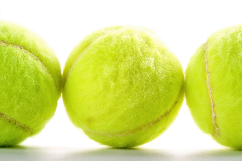 Three tennis balls arranged in a row on a white surface