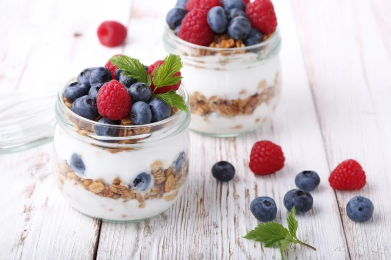 Two glass jars with layered yogurt, granola and berries on a wooden table