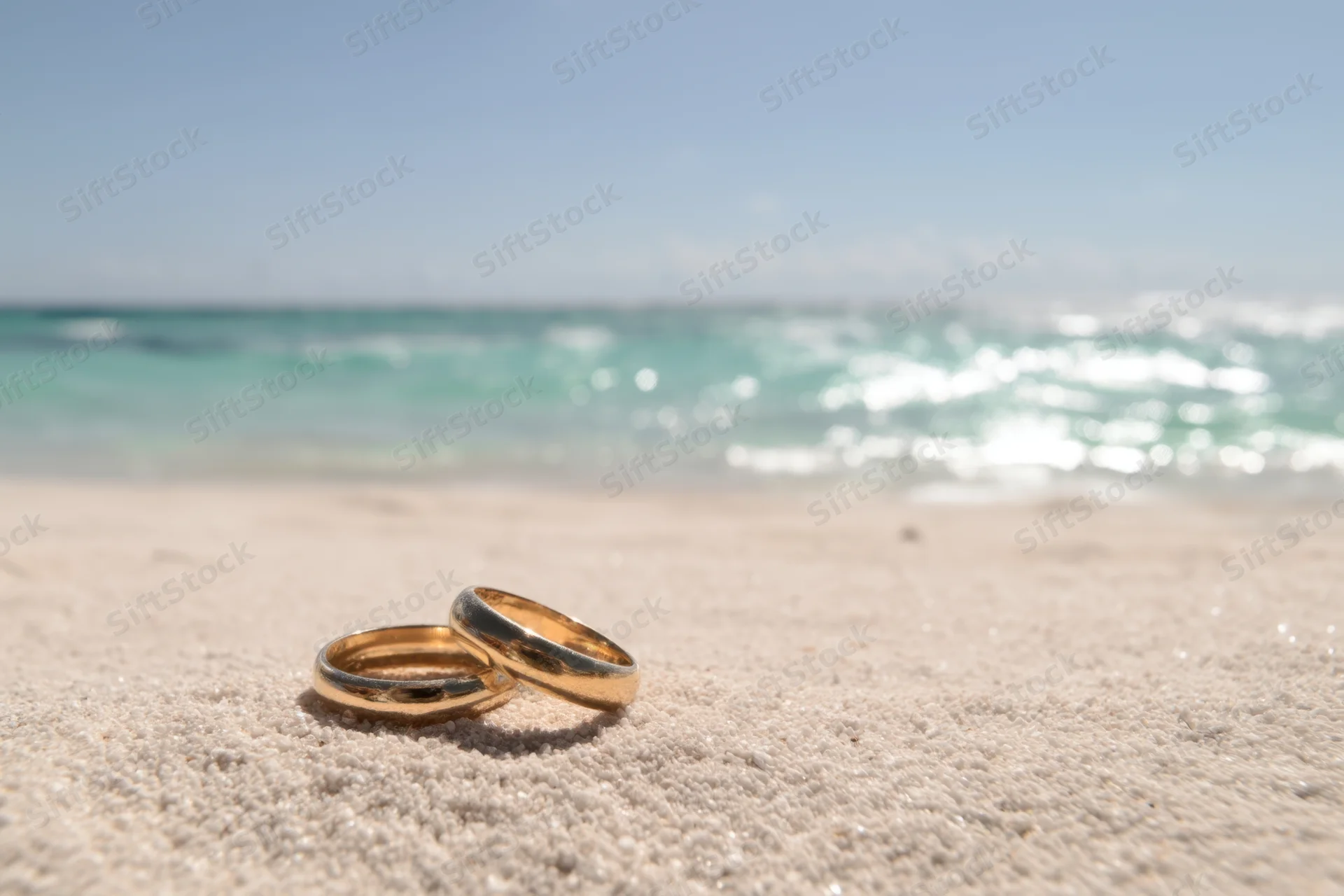 Two golden wedding rings resting on sandy beach near ocean waves
