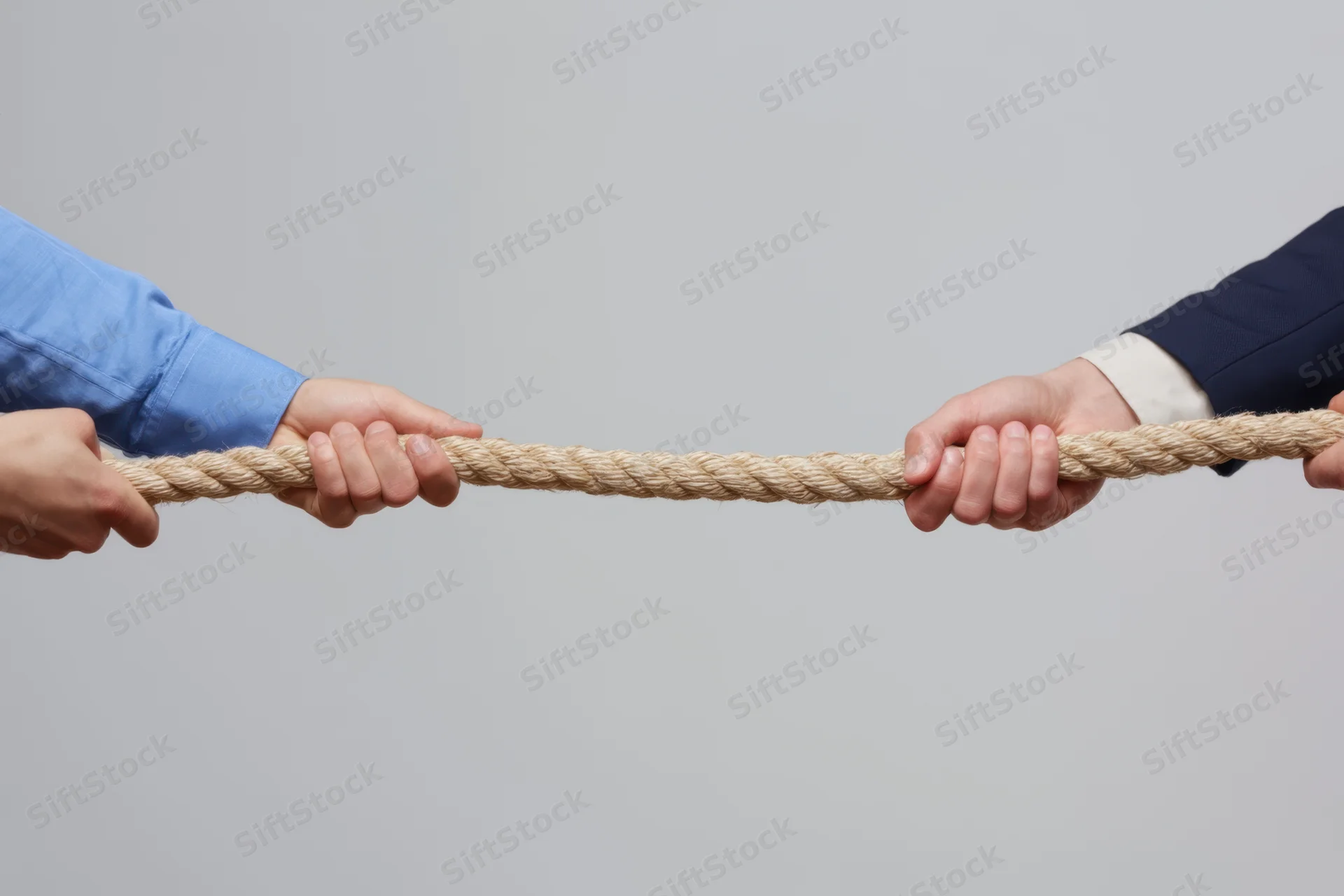 Two pairs of hands gripping a rope in a tug-of-war against a plain gray background