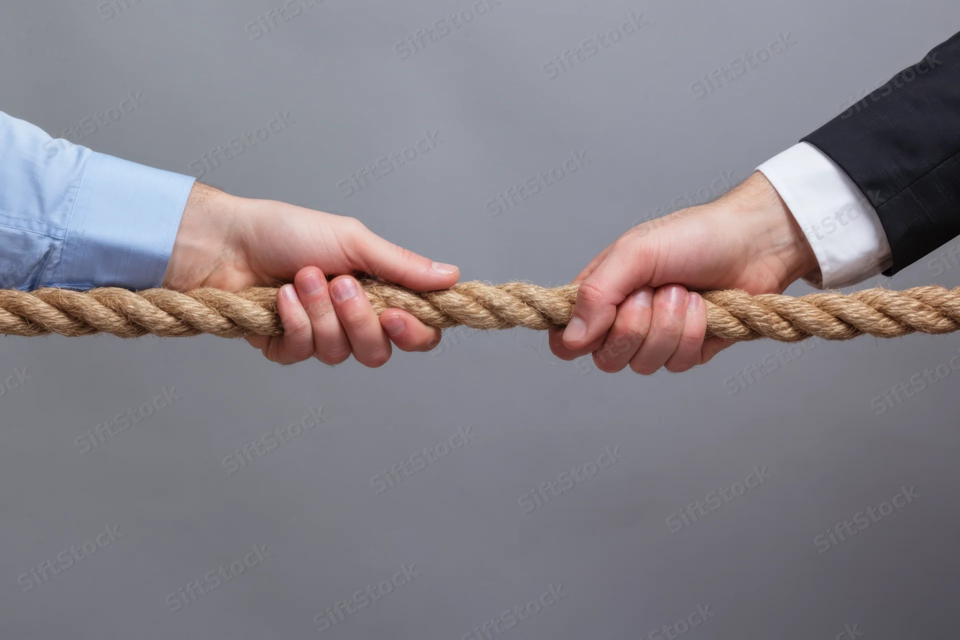 Two hands gripping a rope in a tug-of-war against a gray background
