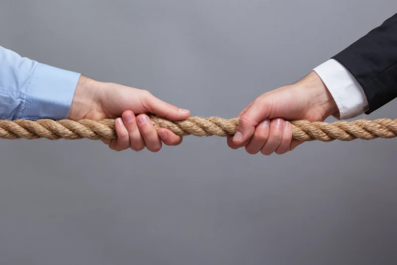 Two hands gripping a rope in a tug-of-war against a gray background
