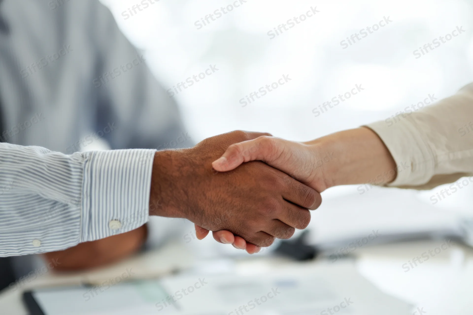 Two people shaking hands across a desk in an office setting