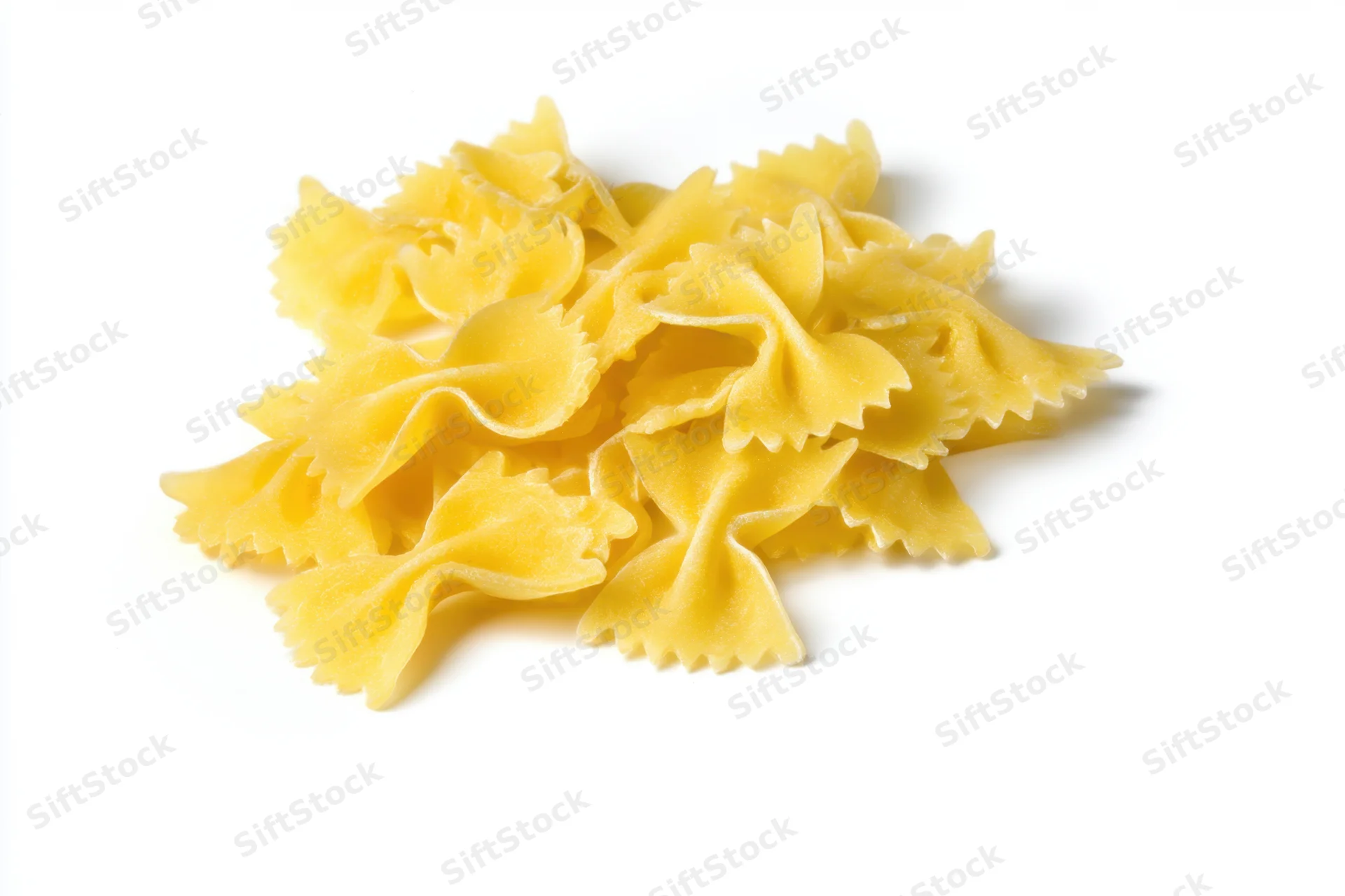 Uncooked farfalle pasta pieces scattered on a white surface