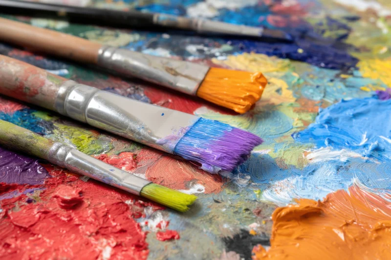 Paintbrushes resting on a colorful palette covered in mixed paint