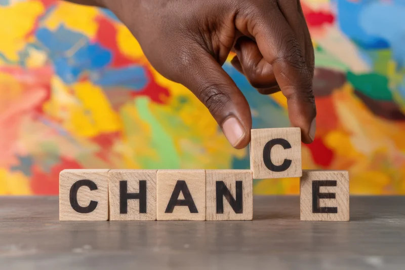 Hand repositioning wooden letter blocks spelling chance on a table with colorful abstract background