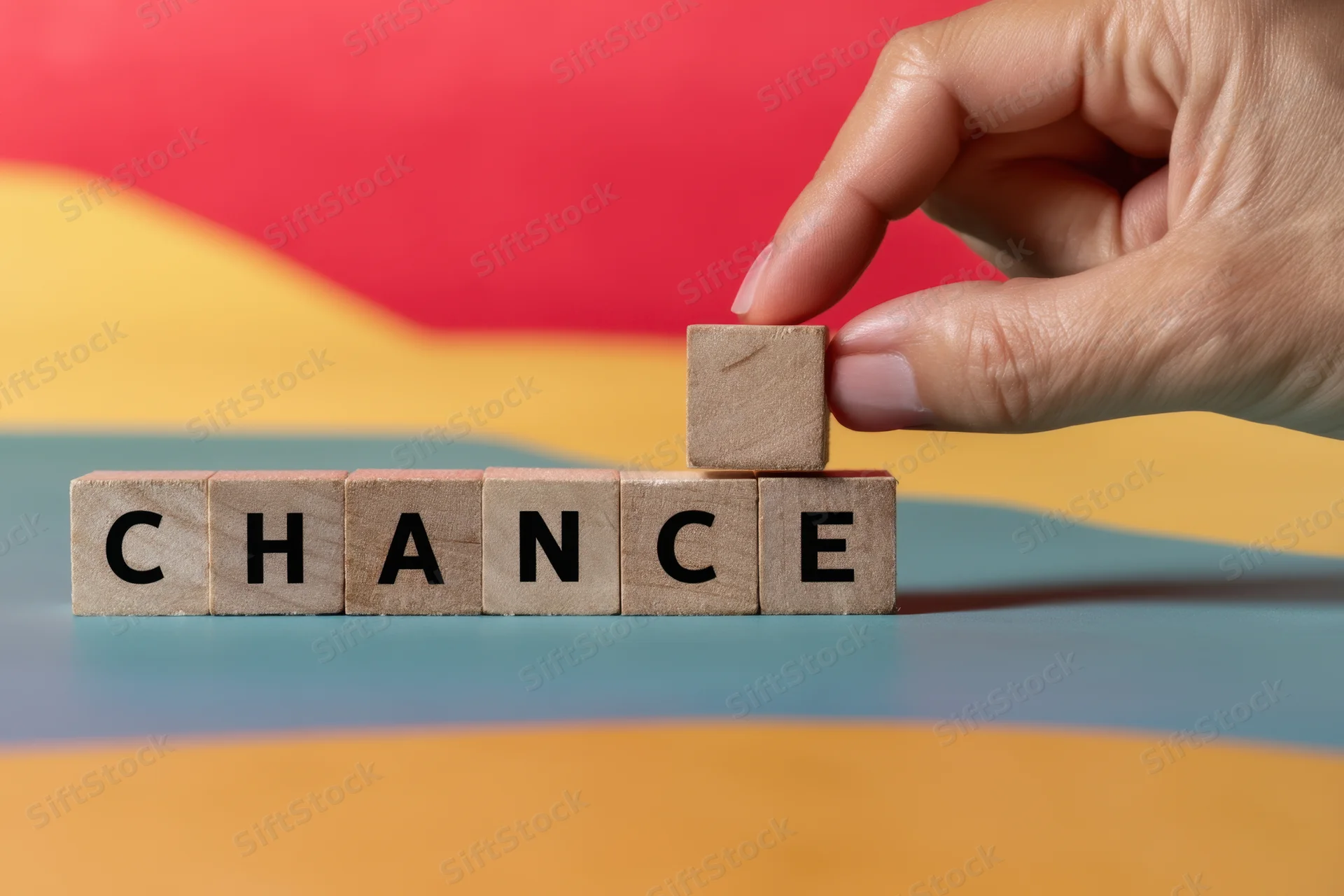 Hand repositioning wooden letter blocks spelling chance on a colorful surface