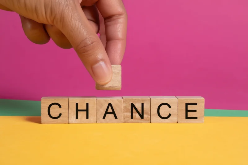 Hand rearranging wooden letter blocks spelling chance on a colorful surface