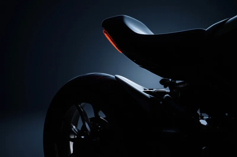 Sleek rear profile of a modern motorcycle in dark studio lighting with red tail light illuminated