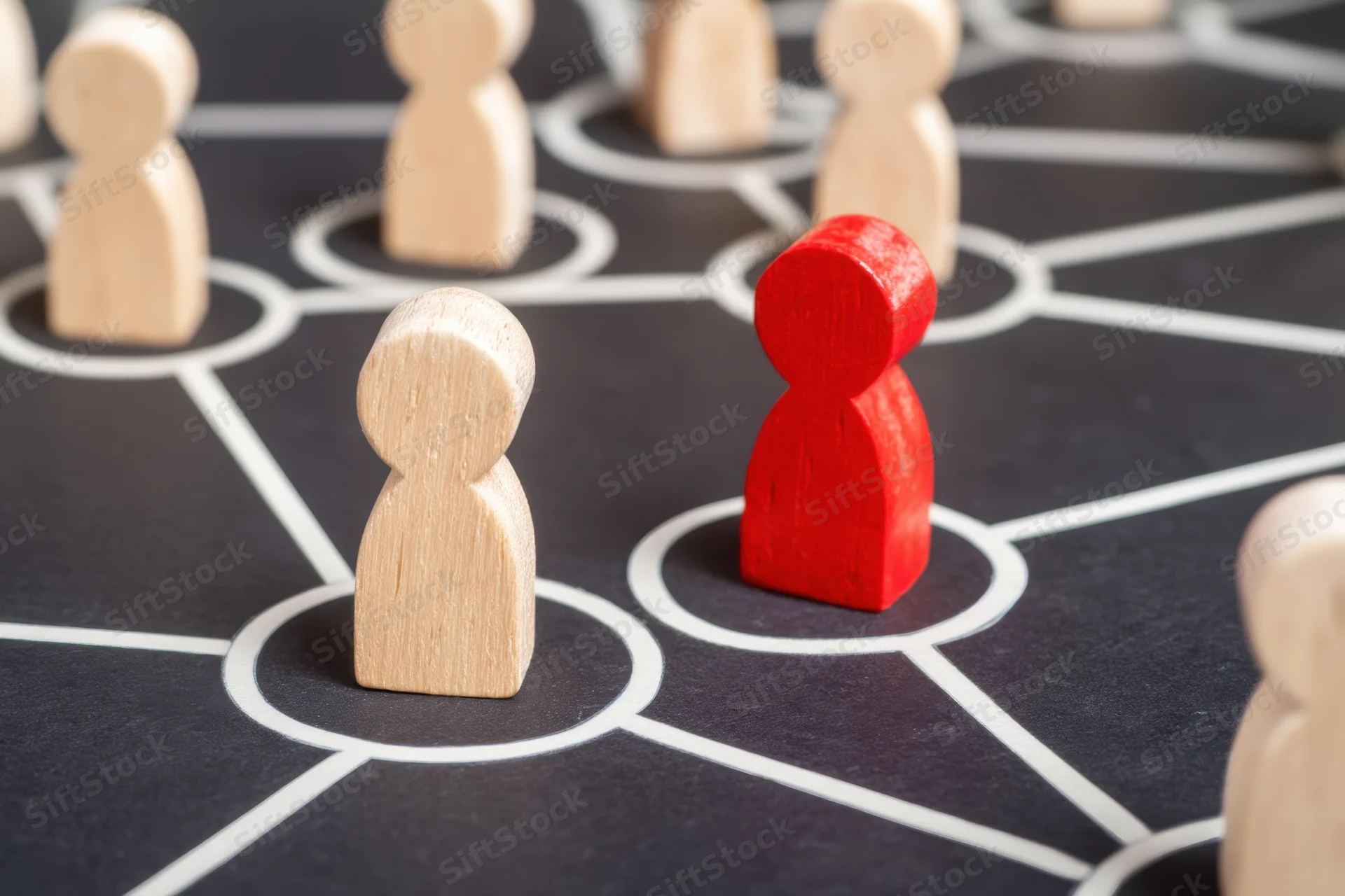 Wooden figures arranged on a network grid with one red figure among beige ones