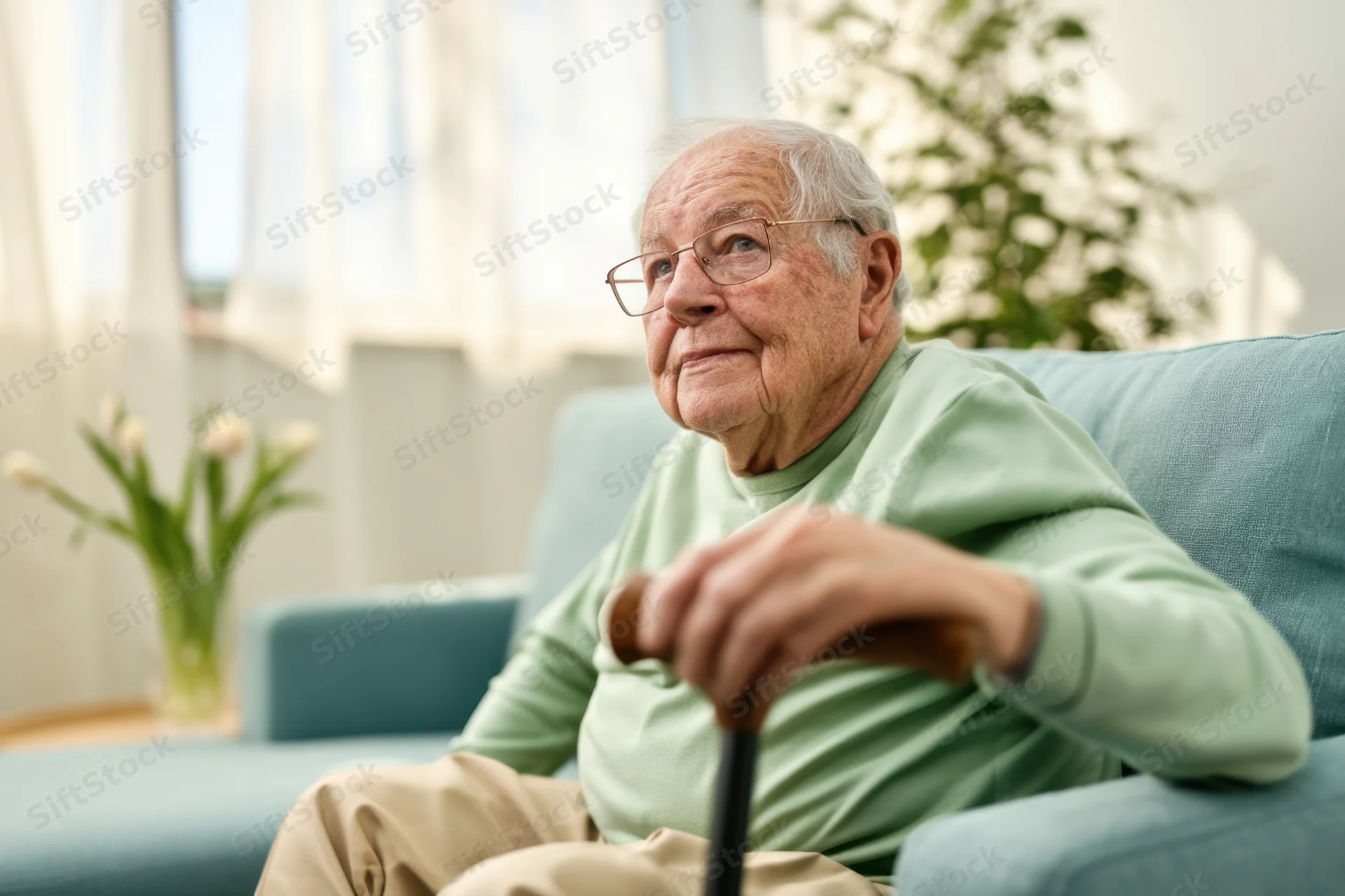 Elderly man sitting on sofa holding cane in living room