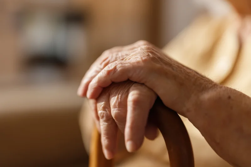Elderly hands resting on a wooden cane handle