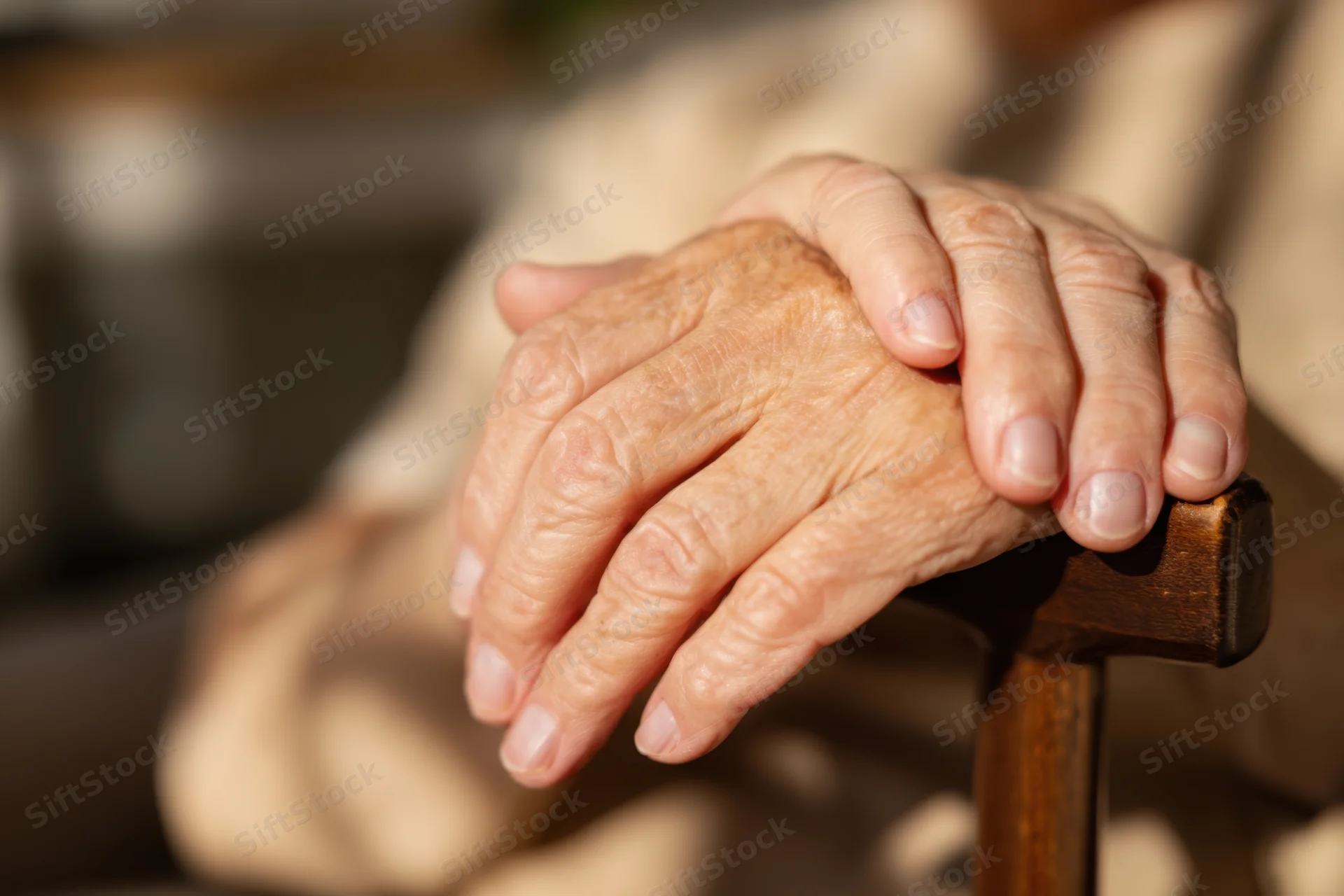Elderly hands resting on a wooden cane outdoors in sunlight