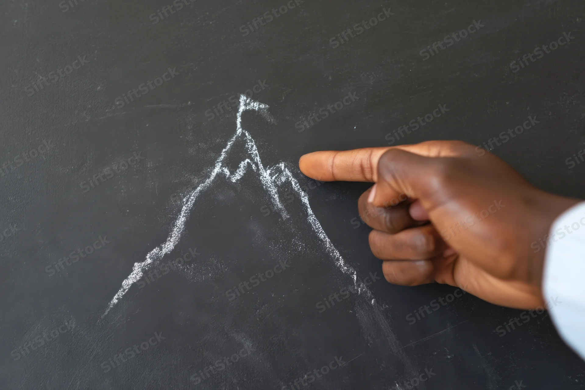 Hand pointing to chalk-drawn mountain on blackboard in classroom setting