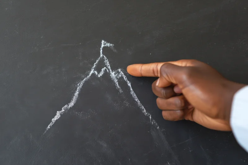 Hand pointing to chalk-drawn mountain on blackboard in classroom setting
