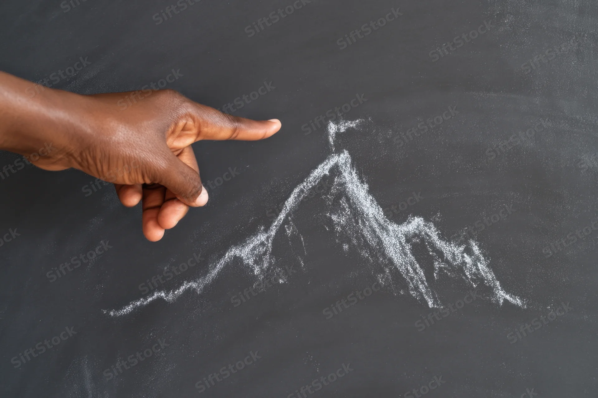 Hand pointing to chalk-drawn mountain on blackboard