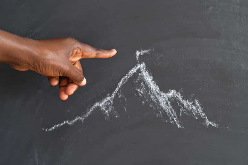 Hand pointing to chalk-drawn mountain on blackboard