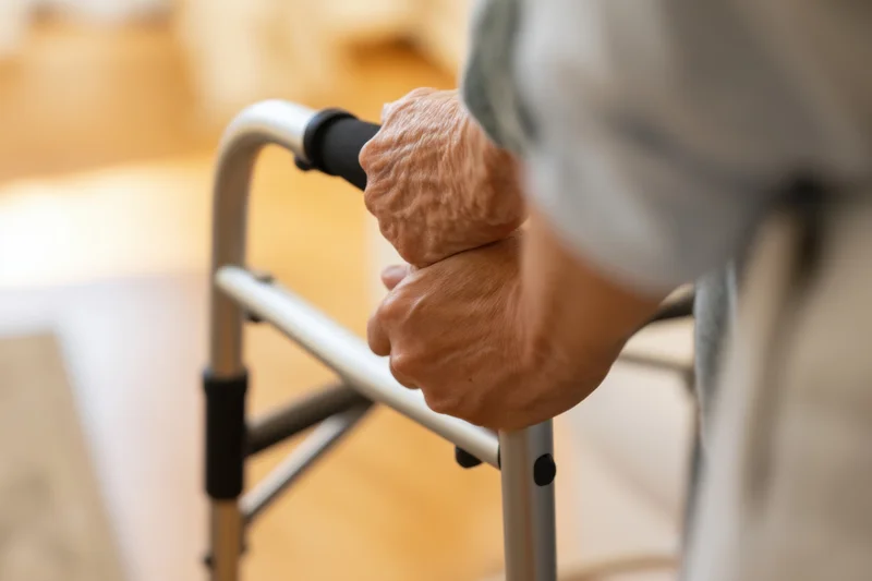 Senior hands gripping walker frame for support indoors