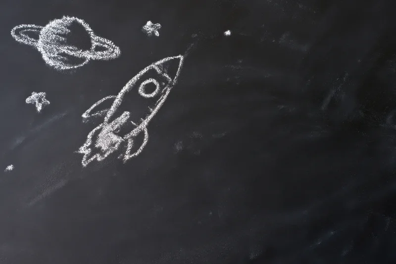Chalk drawing of a rocket ship flying through space with planets and stars on a blackboard