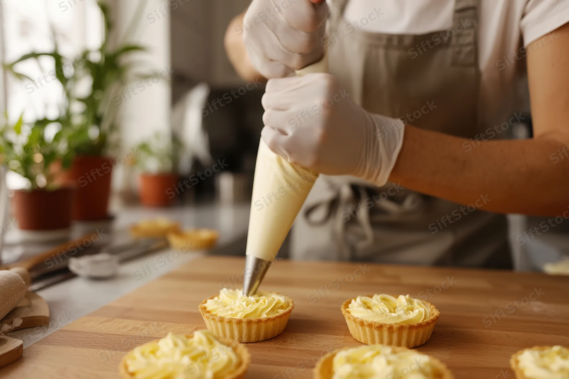 Baker piping cream into small tarts on a wooden kitchen table