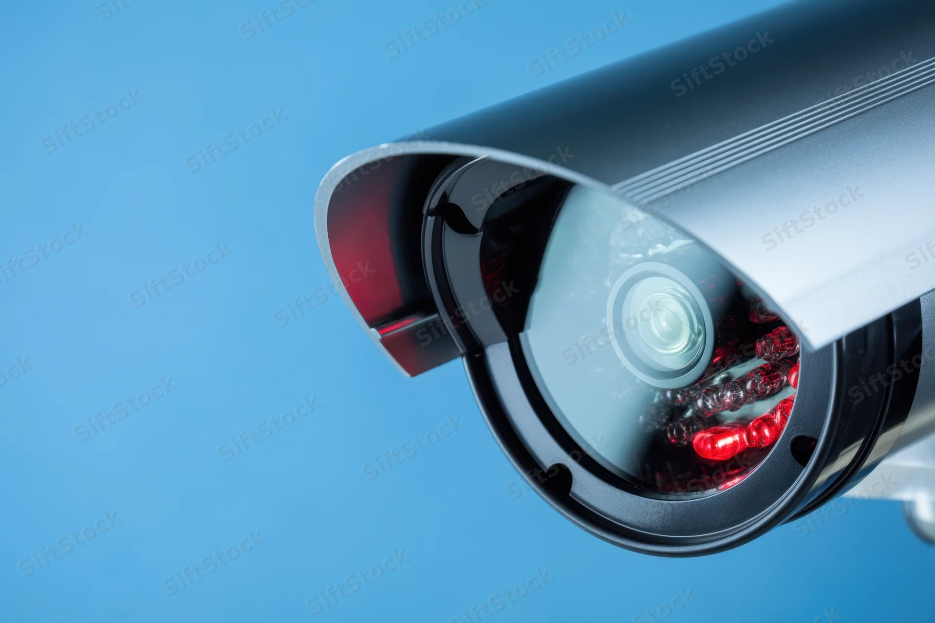 Close-up of a glossy silver cctv camera with red infrared leds against a blue background