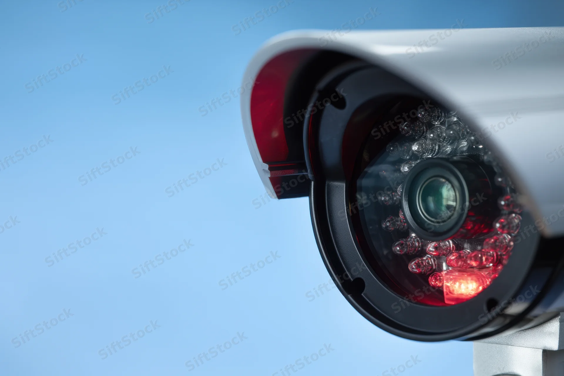 Close-up of a silver cctv camera with red led lights against a blue sky background