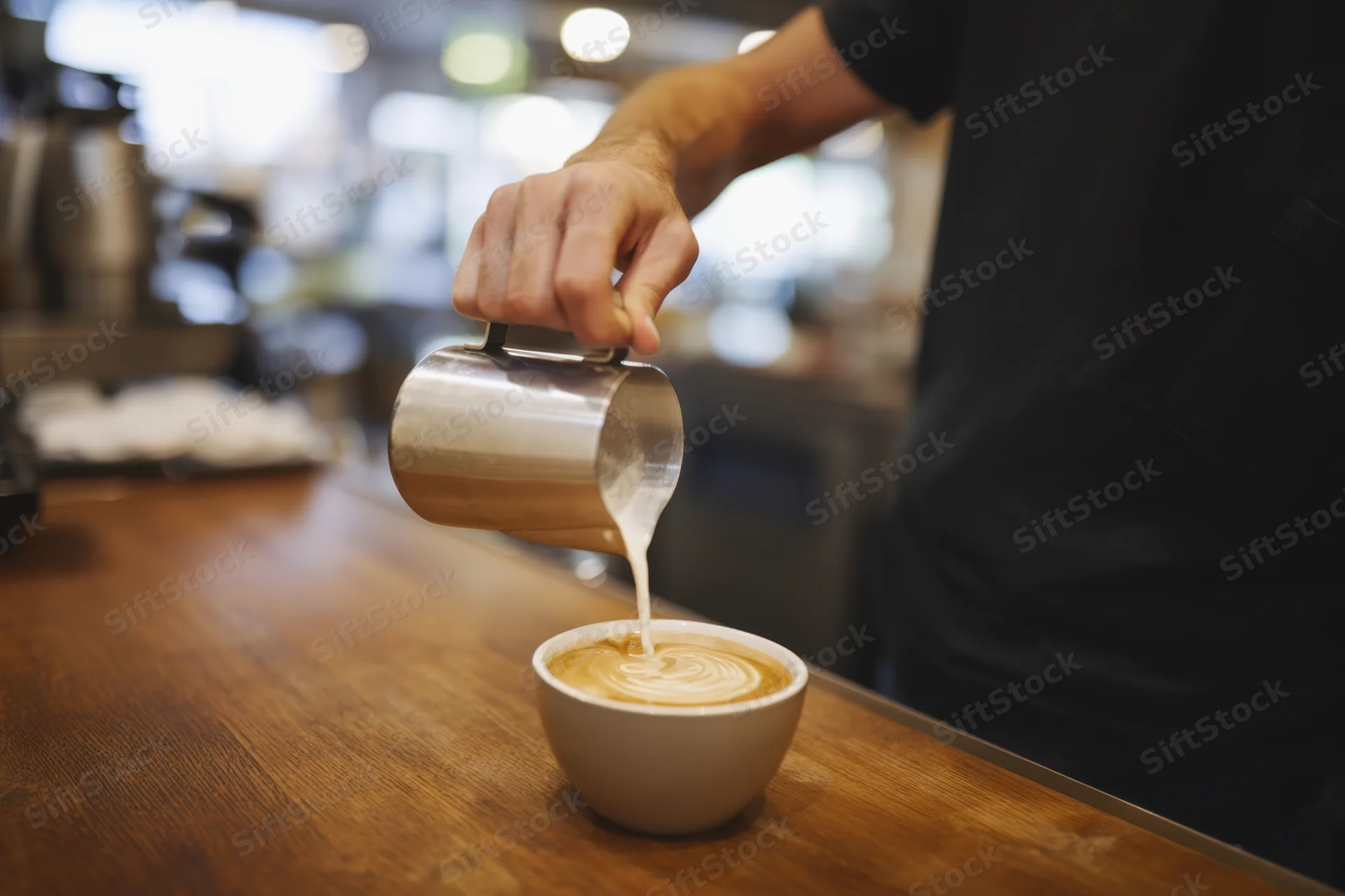 Barista pouring steamed milk into a latte on a wooden counter in a cafe