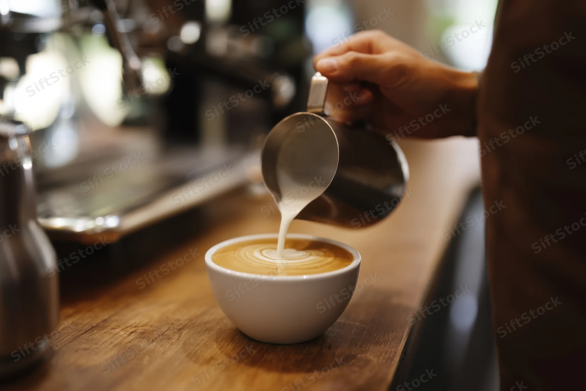 Barista pouring steamed milk into a cup of coffee on a wooden counter in a cafe
