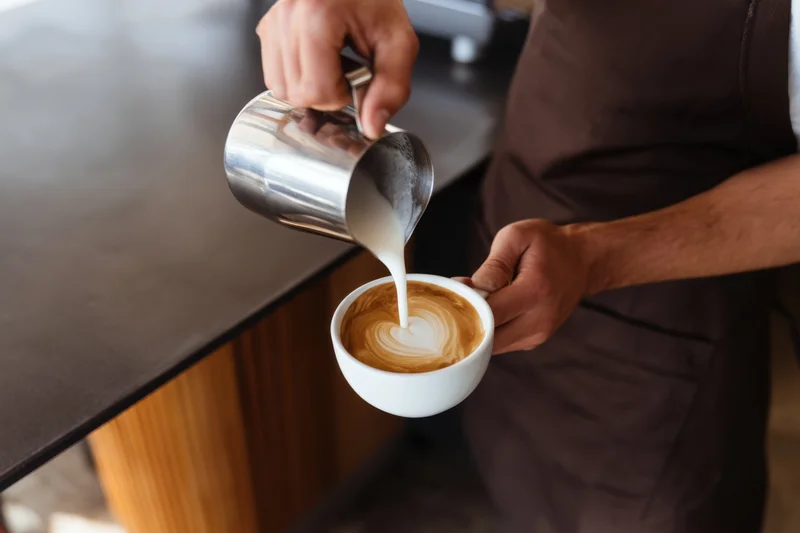 Barista pouring steamed milk into a latte cup to create latte art at a cafe counter