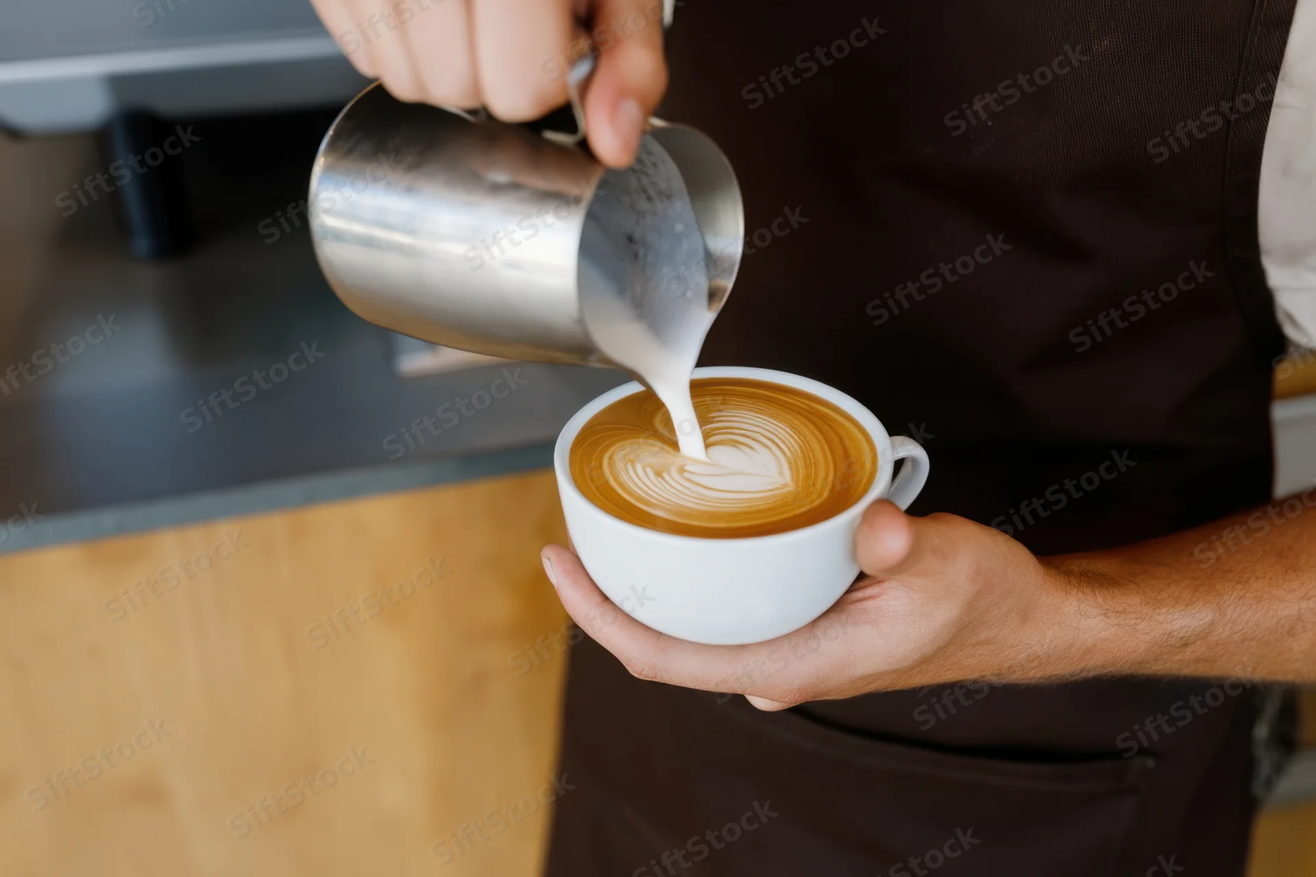Barista pouring steamed milk into a latte to create latte art in a coffee shop