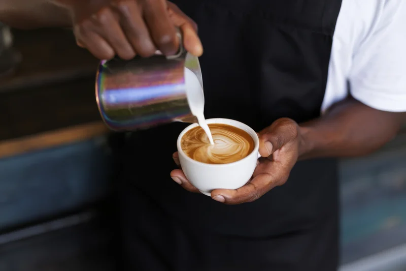 Barista pouring steamed milk into a latte cup to create latte art in a coffee shop