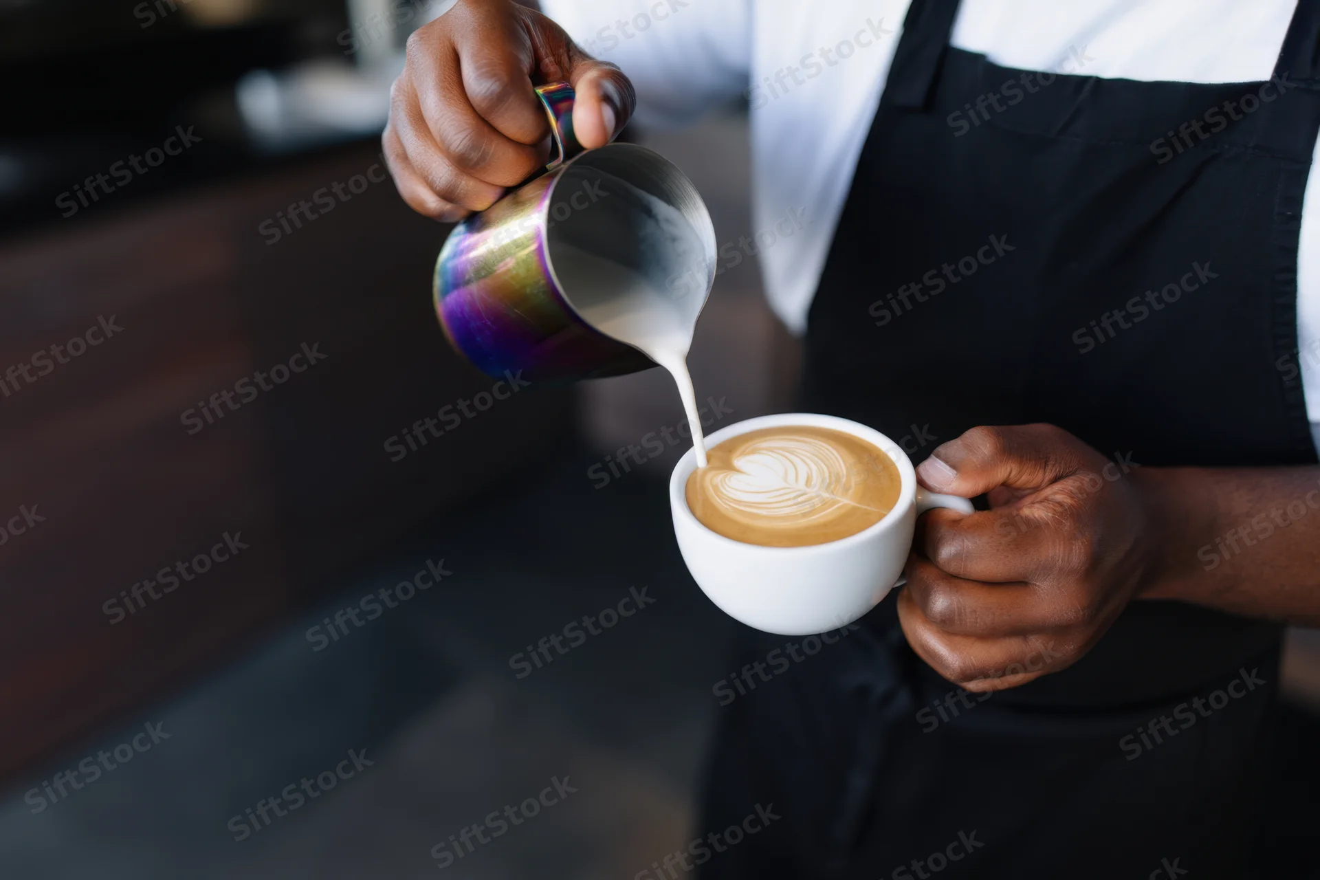 Barista pouring steamed milk into a latte to create latte art in a coffee shop