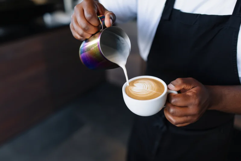 Barista pouring steamed milk into a latte to create latte art in a coffee shop