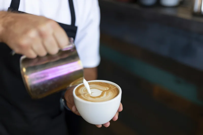 Barista pouring steamed milk into a latte cup to create latte art in a coffee shop