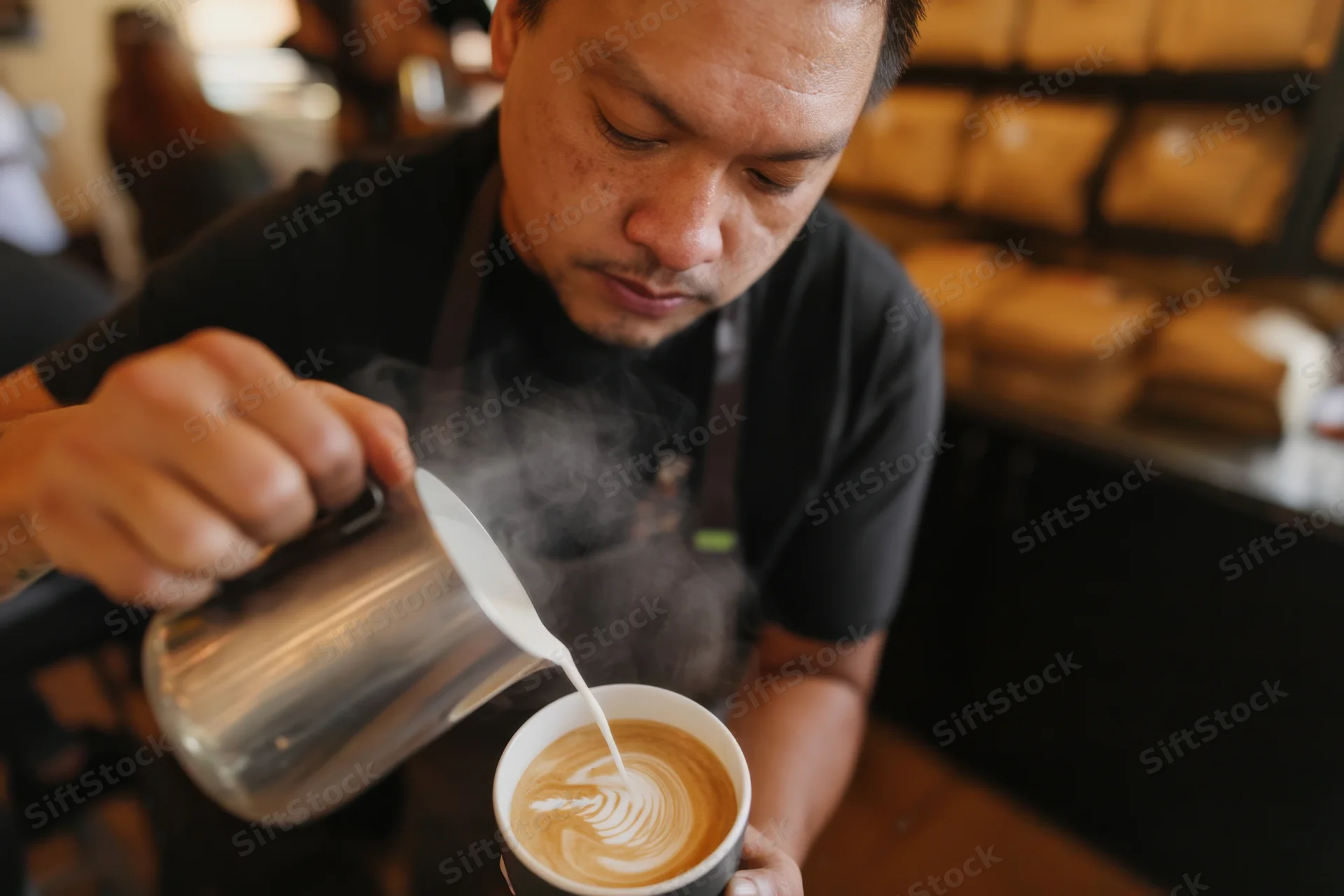 Barista pouring steamed milk into a latte cup to create latte art in a coffee shop