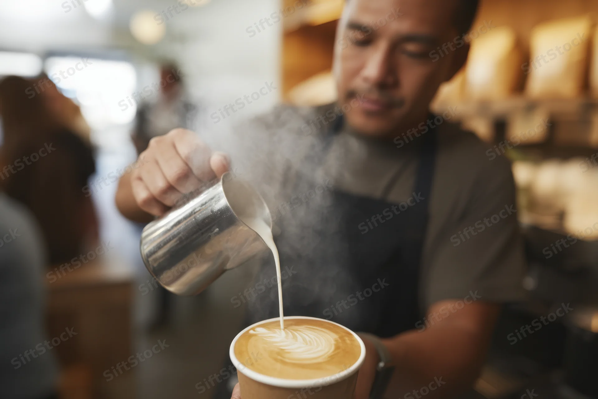 Barista pouring steamed milk into a latte cup to create latte art in a coffee shop