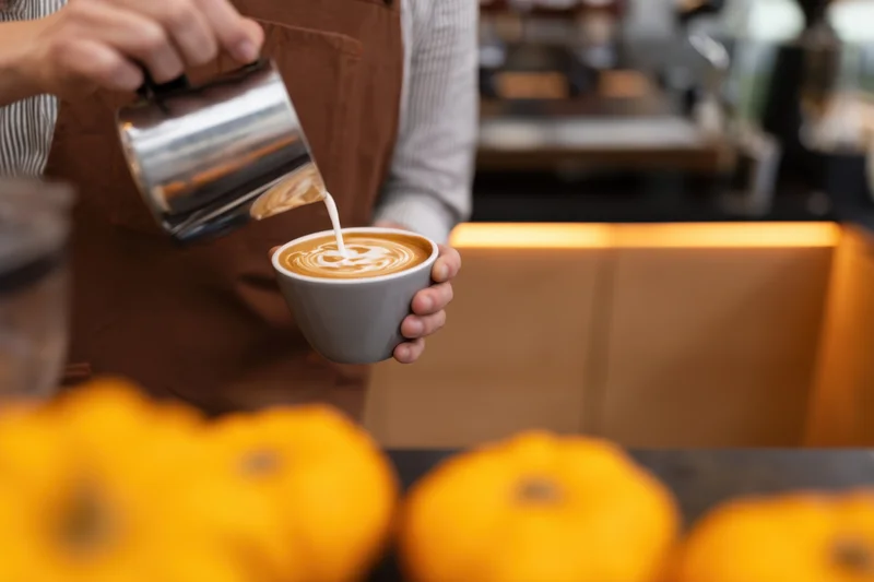 Barista pouring steamed milk into a latte cup with pumpkin decor in foreground