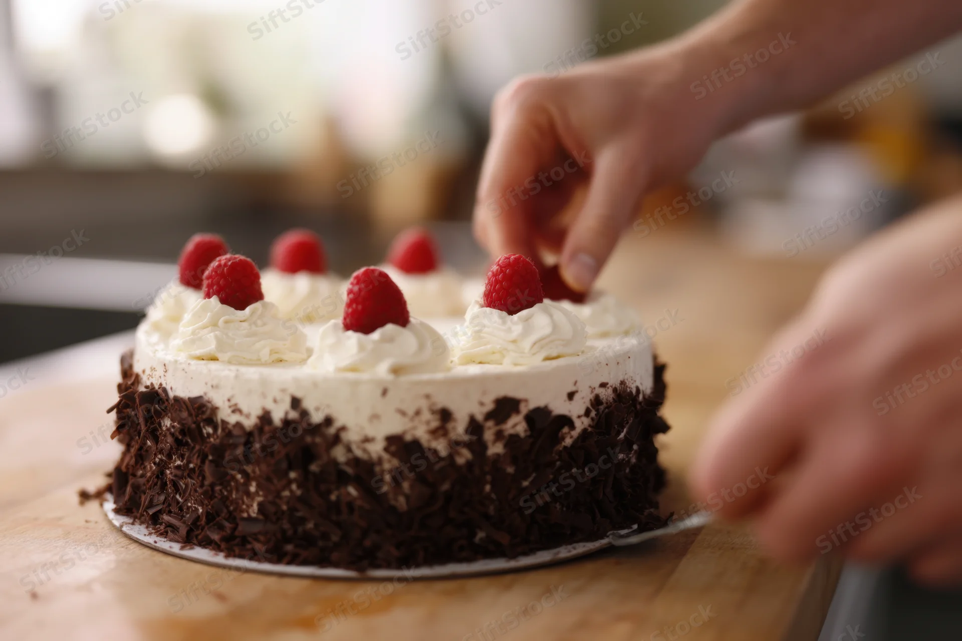 Man garnishing chocolate cake with raspberries on wooden cutting board
