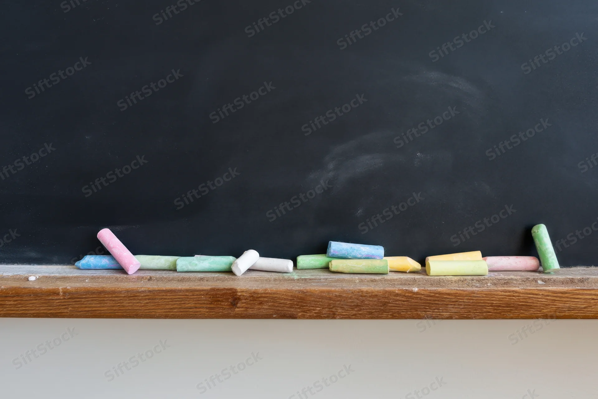 Colorful chalk pieces scattered on wooden ledge of black chalkboard in classroom