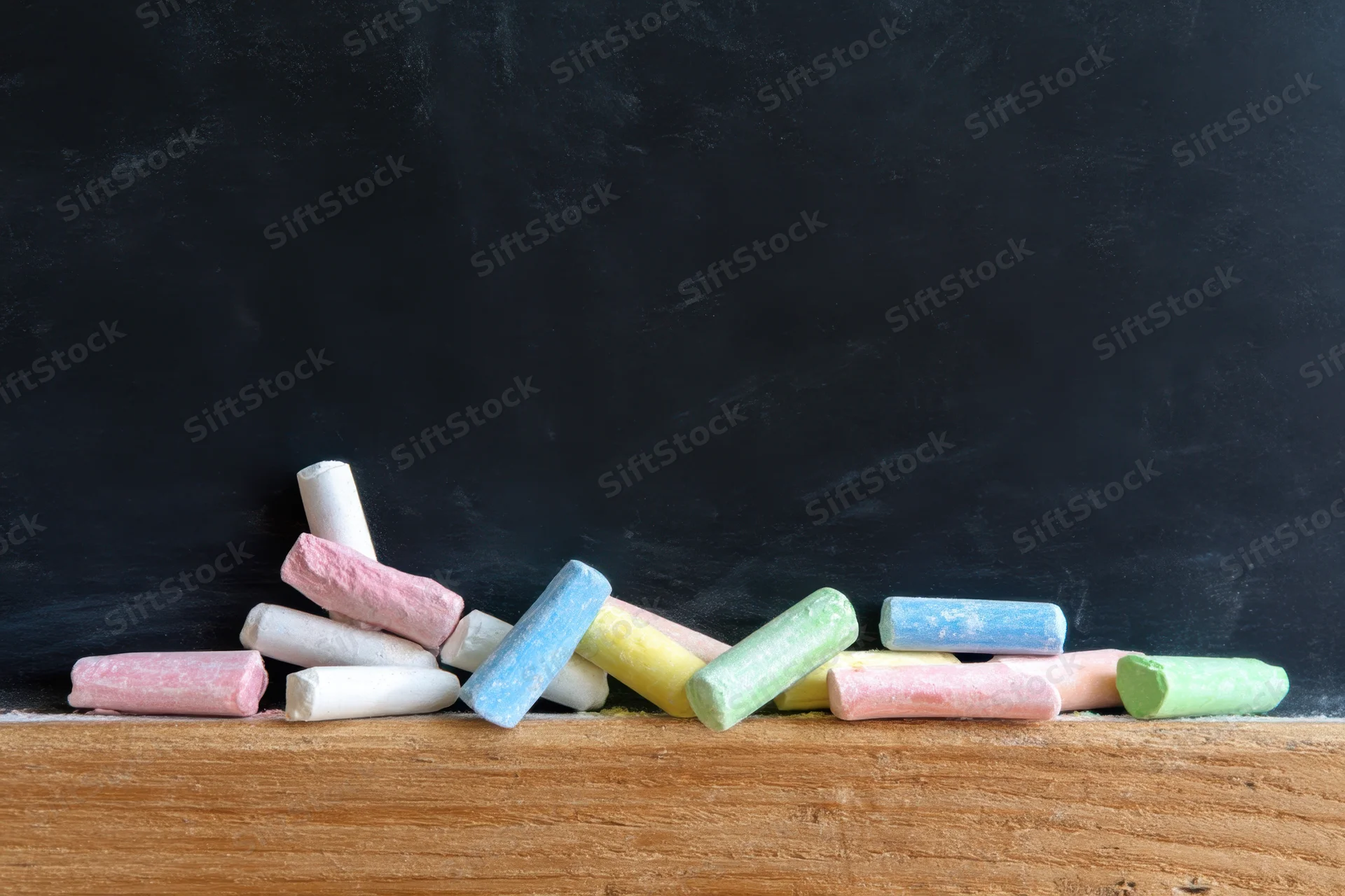 Colorful chalk pieces scattered on a wooden ledge in front of a black chalkboard