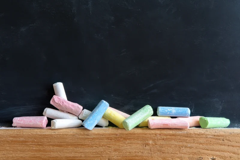 Colorful chalk pieces scattered on a wooden ledge in front of a black chalkboard