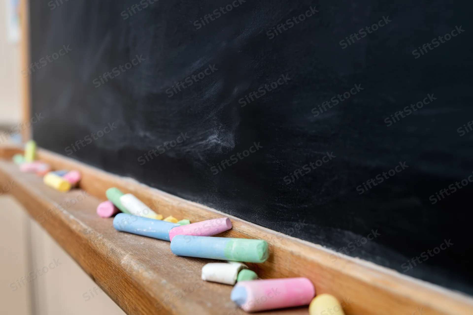 Colorful chalk pieces scattered on wooden ledge of black chalkboard in classroom