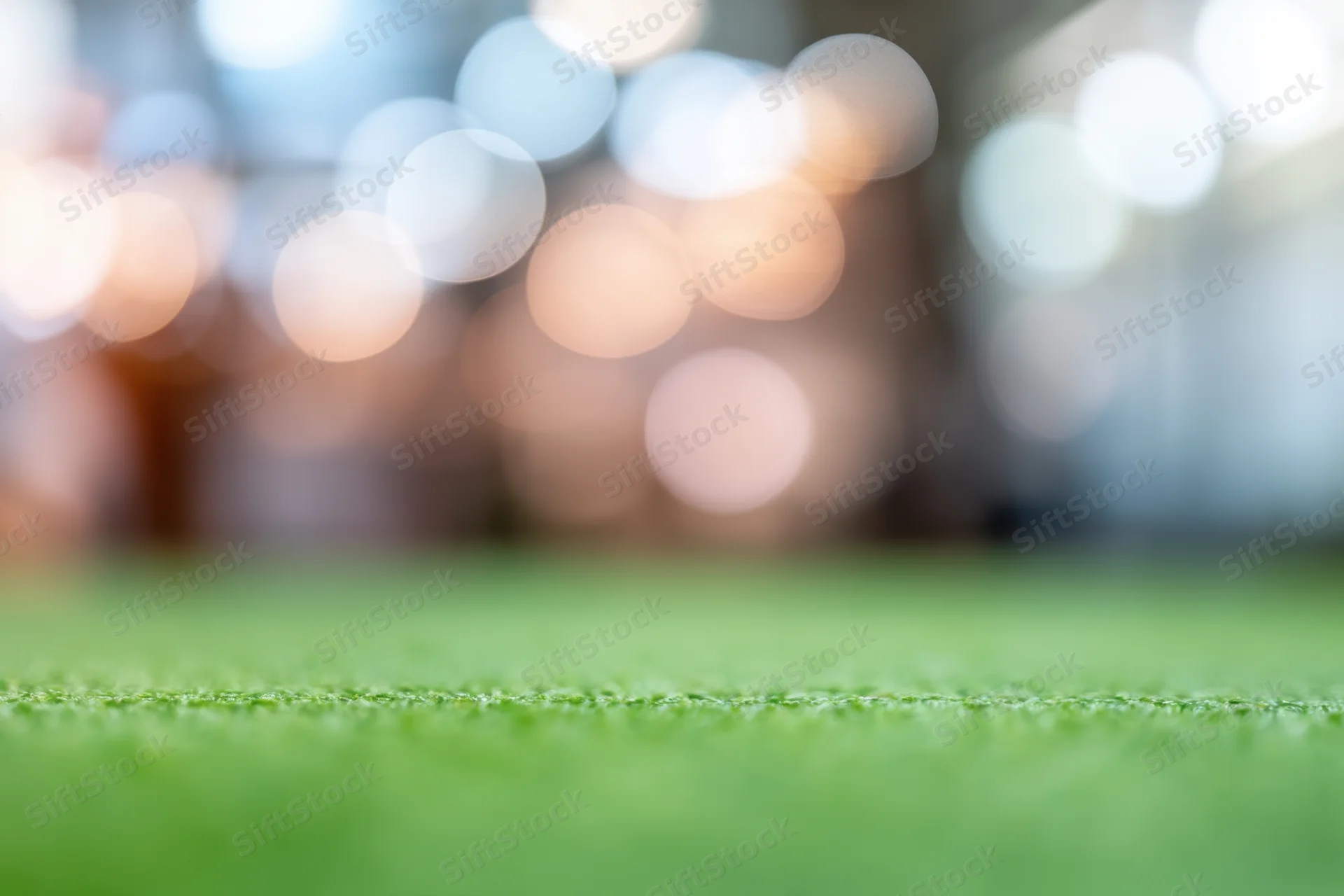 Close-up of green grass field with blurred bokeh lights in background