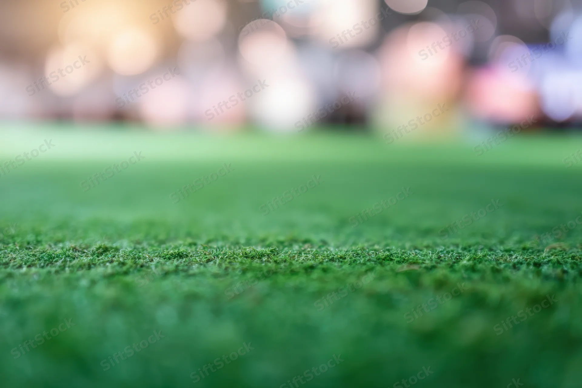 Close-up of green grass field with blurred bokeh lights in background